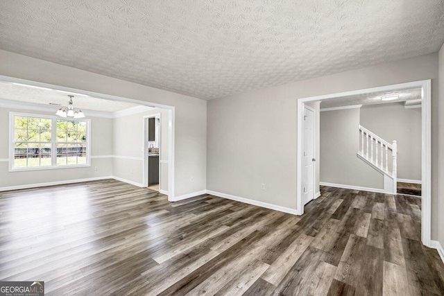 empty room with a textured ceiling, an inviting chandelier, stairway, and dark wood-style flooring