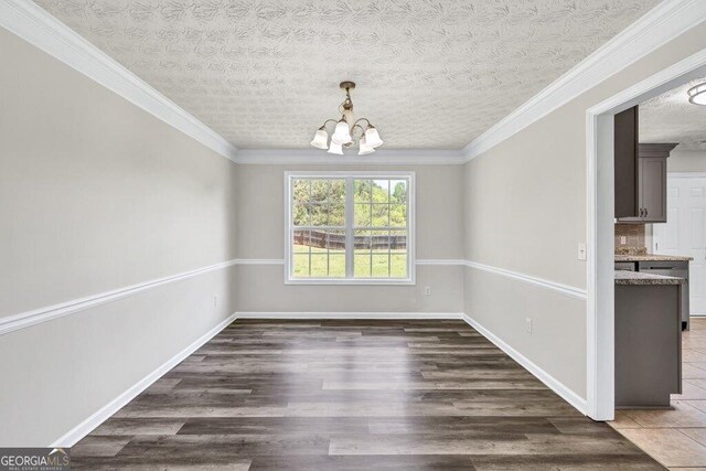 unfurnished dining area featuring crown molding, baseboards, a notable chandelier, and wood finished floors