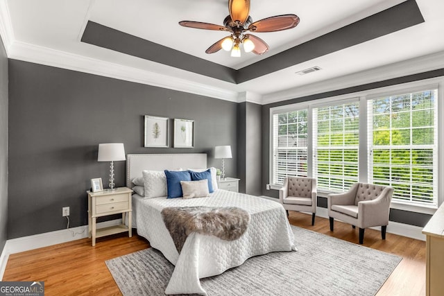 bedroom featuring light wood finished floors, visible vents, a tray ceiling, and ornamental molding