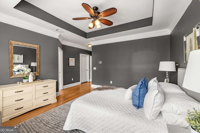 bedroom featuring baseboards, light wood-style flooring, crown molding, visible vents, and a tray ceiling