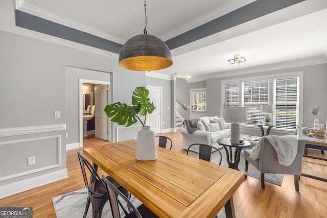 dining area featuring light wood-style flooring, crown molding, baseboards, and stairway