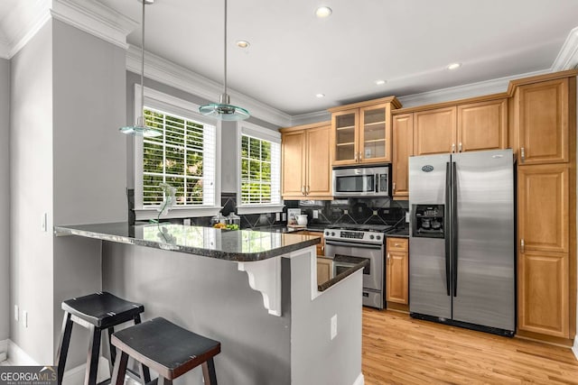 kitchen featuring glass insert cabinets, a peninsula, ornamental molding, a breakfast bar, and stainless steel appliances