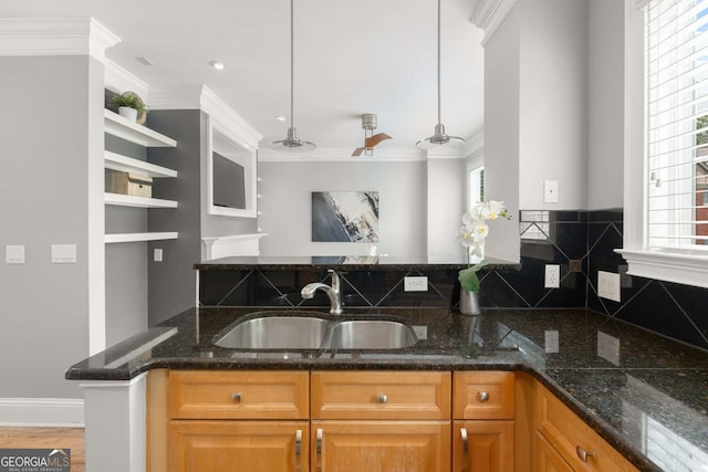 kitchen featuring plenty of natural light, ornamental molding, a sink, and dark stone counters