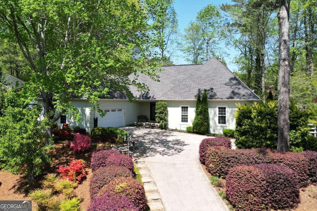 view of front of property featuring an attached garage, roof with shingles, concrete driveway, and stucco siding