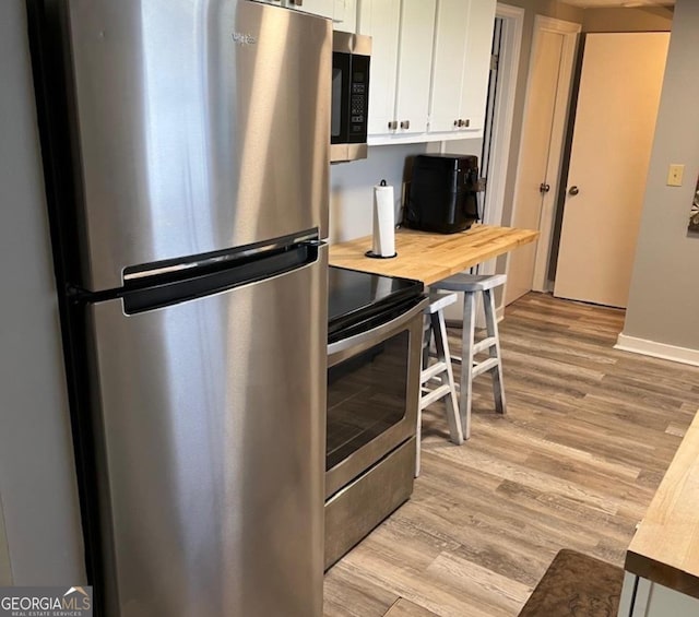 kitchen with wooden counters, baseboards, white cabinetry, light wood-style flooring, and stainless steel appliances