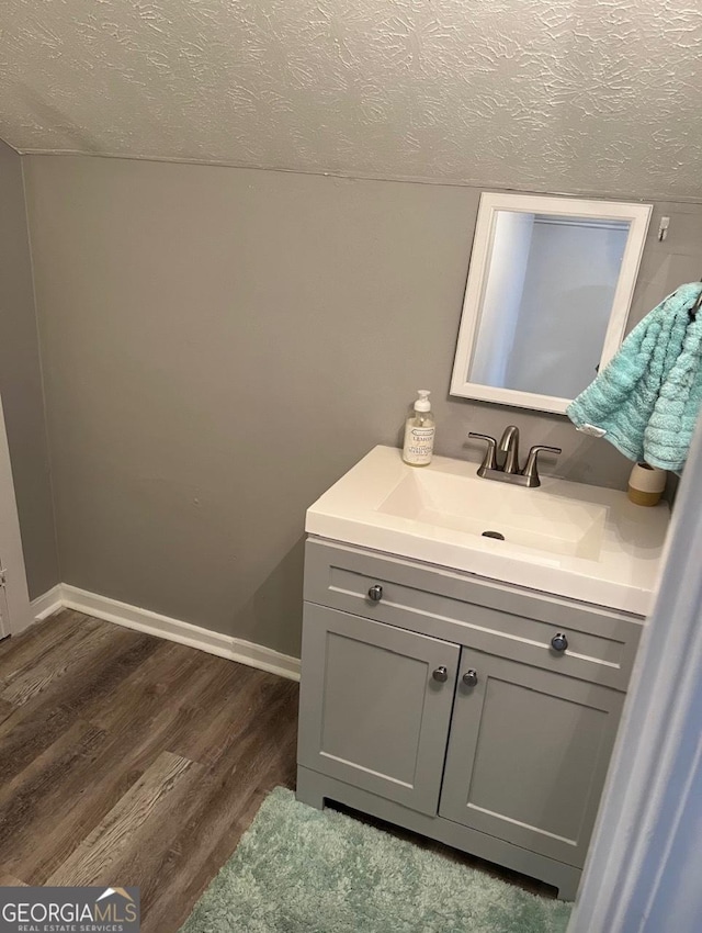 bathroom with vanity, baseboards, a textured ceiling, and wood finished floors