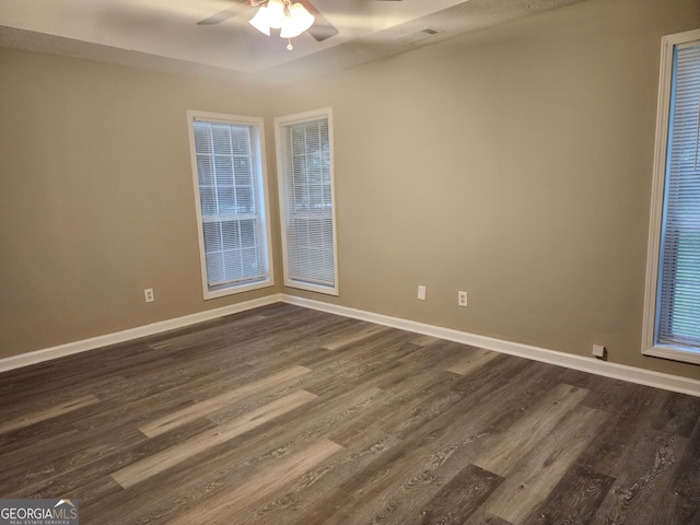 empty room featuring visible vents, baseboards, a ceiling fan, and dark wood finished floors