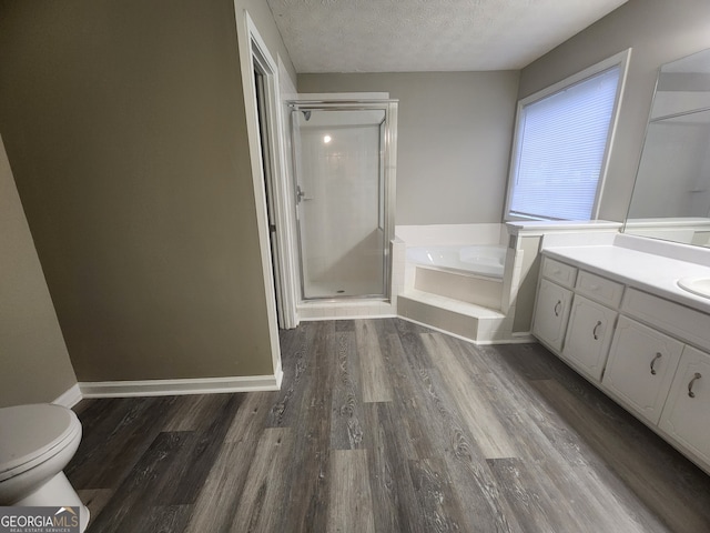 full bathroom featuring a textured ceiling, vanity, toilet, wood finished floors, and a stall shower