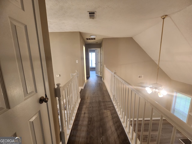 hall with visible vents, an upstairs landing, wood finished floors, and a healthy amount of sunlight