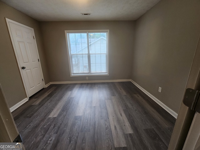 empty room featuring visible vents, dark wood-style floors, and a textured ceiling