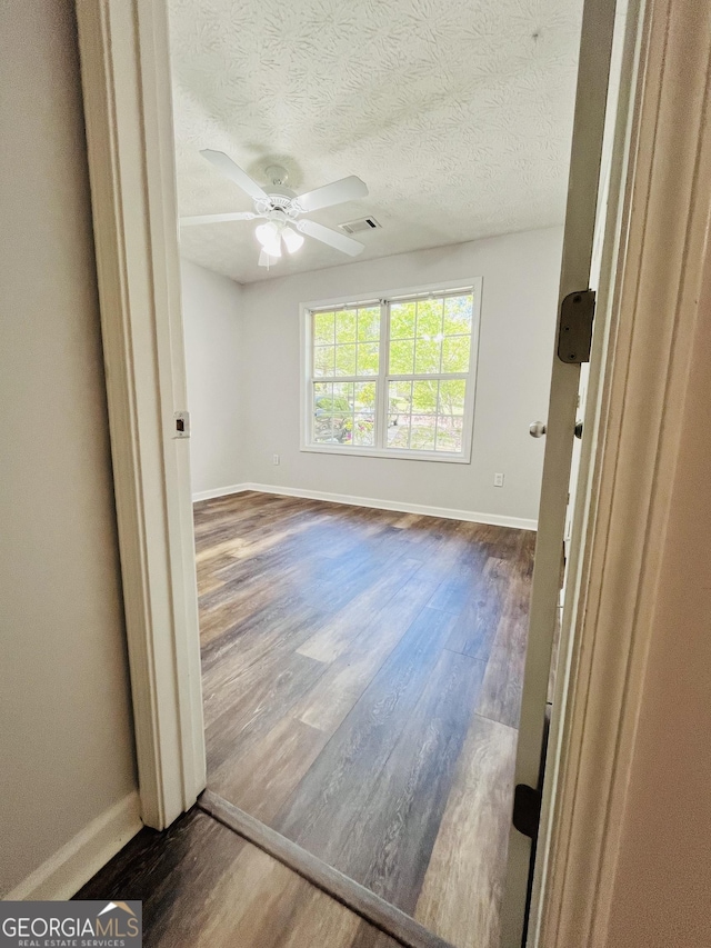 spare room with visible vents, baseboards, a ceiling fan, and dark wood-style floors