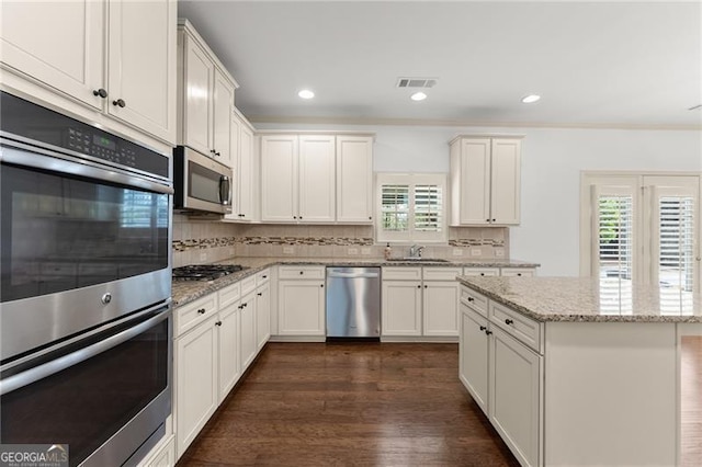 kitchen featuring visible vents, a sink, dark wood-style floors, stainless steel appliances, and backsplash