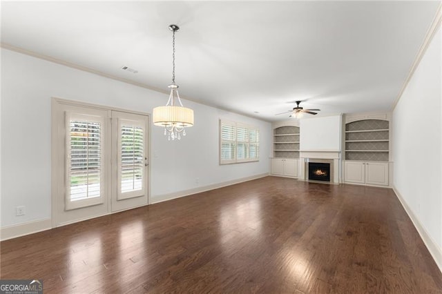 unfurnished living room featuring built in features, a lit fireplace, wood finished floors, and ceiling fan with notable chandelier