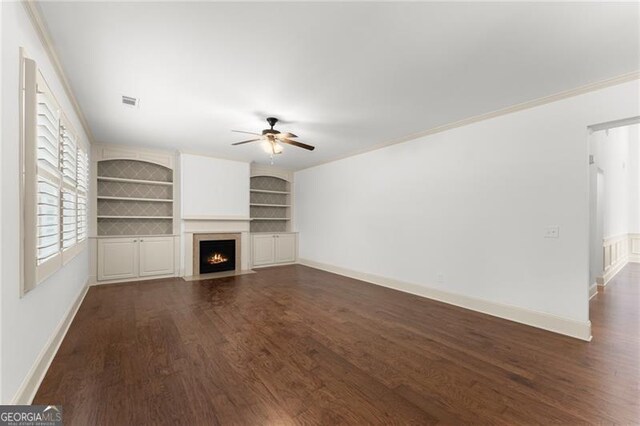 unfurnished living room with dark wood-style flooring, baseboards, a fireplace with flush hearth, ceiling fan, and built in shelves