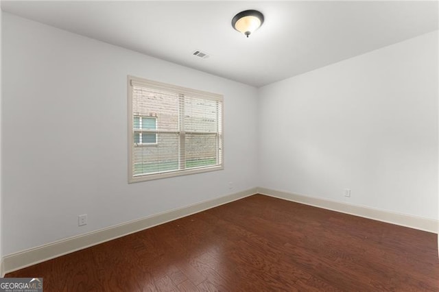 empty room featuring visible vents, baseboards, and dark wood-style floors