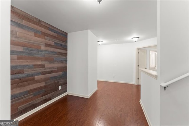 unfurnished room with wood finished floors, wooden walls, baseboards, and an accent wall