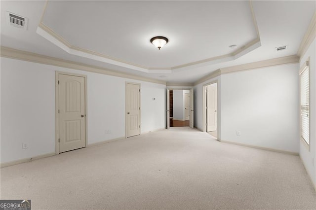carpeted spare room with a wealth of natural light, visible vents, crown molding, and a raised ceiling