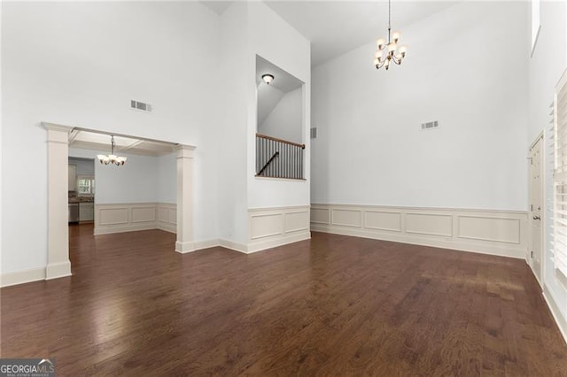 unfurnished dining area with visible vents, a decorative wall, a chandelier, wood finished floors, and a towering ceiling