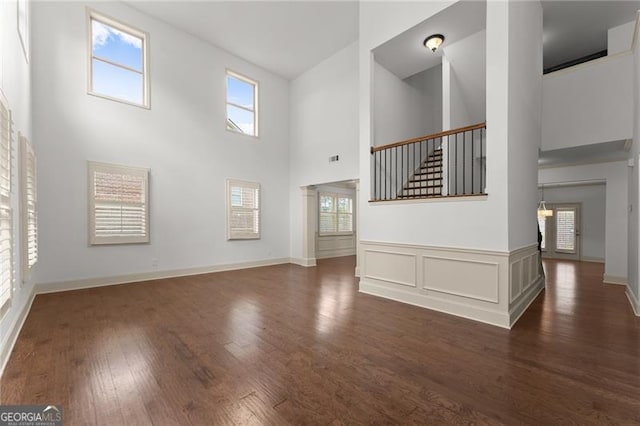unfurnished living room featuring a wealth of natural light, a towering ceiling, and dark wood-style floors