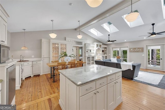 934 Pine Cir, Woodstock, GA 30189 - kitchen with light wood-type flooring, vaulted ceiling with skylight, white cabinets, stainless steel appliances, and hanging light fixtures