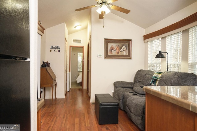 sitting room with vaulted ceiling, a ceiling fan, wood finished floors, and visible vents