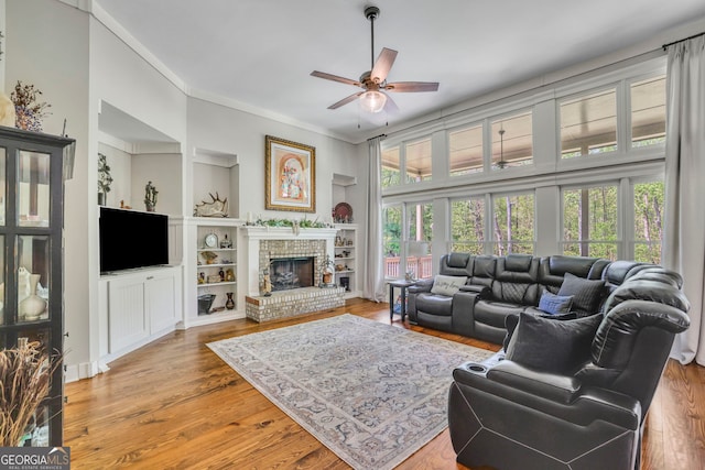 living area featuring ceiling fan, ornamental molding, wood finished floors, and a fireplace