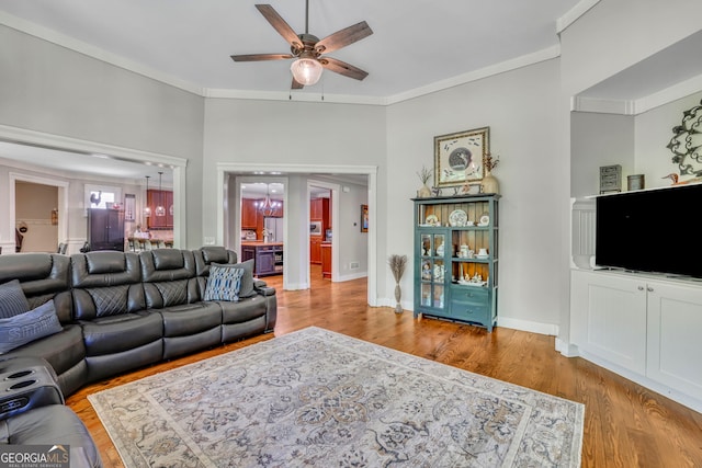 living area featuring a ceiling fan, baseboards, ornamental molding, and wood finished floors