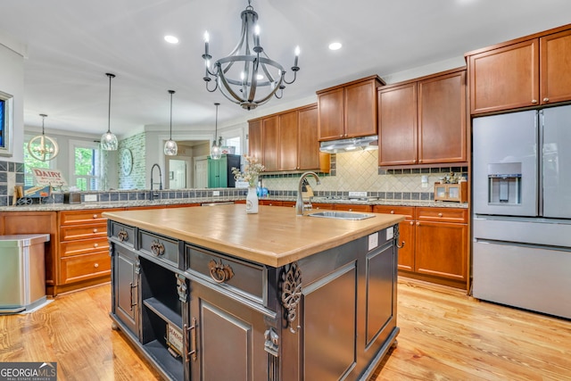 kitchen featuring light wood-style floors, refrigerator with ice dispenser, a center island with sink, and tasteful backsplash