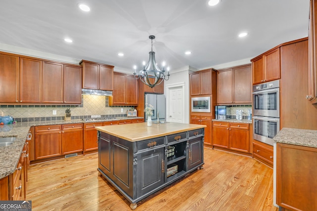 kitchen with pendant lighting, under cabinet range hood, appliances with stainless steel finishes, backsplash, and a notable chandelier