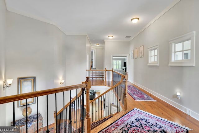 hallway featuring visible vents, wood finished floors, baseboards, an upstairs landing, and ornamental molding