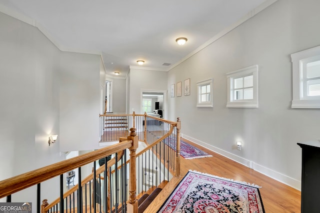 hallway with baseboards, ornamental molding, wood finished floors, and an upstairs landing