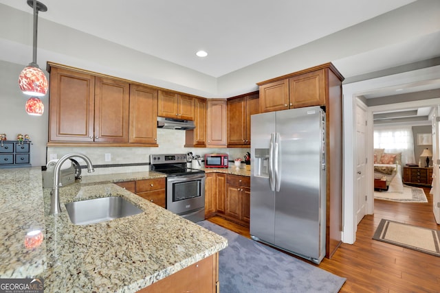 kitchen with a sink, appliances with stainless steel finishes, under cabinet range hood, and brown cabinets