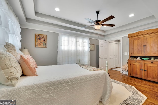 bedroom with recessed lighting, a ceiling fan, a tray ceiling, and light wood-type flooring