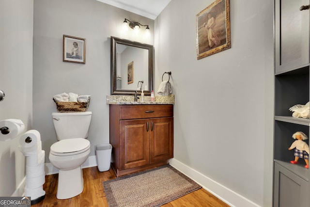 half bathroom with vanity, baseboards, wood finished floors, and toilet