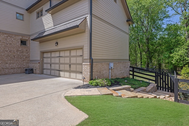 view of side of property featuring an attached garage, fence, a yard, and brick siding