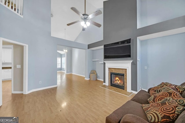 living area with baseboards, a fireplace, a ceiling fan, high vaulted ceiling, and light wood finished floors