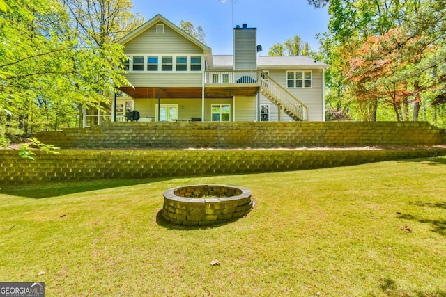back of property with a chimney, a fire pit, stairway, and a lawn