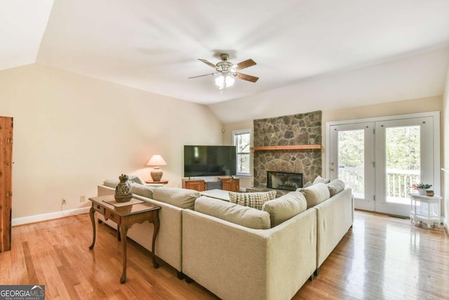 living area with light wood-type flooring, a stone fireplace, vaulted ceiling, and a ceiling fan