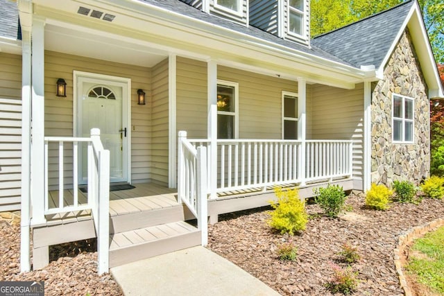 view of exterior entry with a shingled roof, covered porch, and stone siding