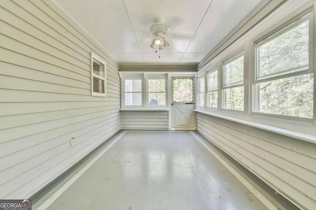 unfurnished sunroom with wood walls and a ceiling fan