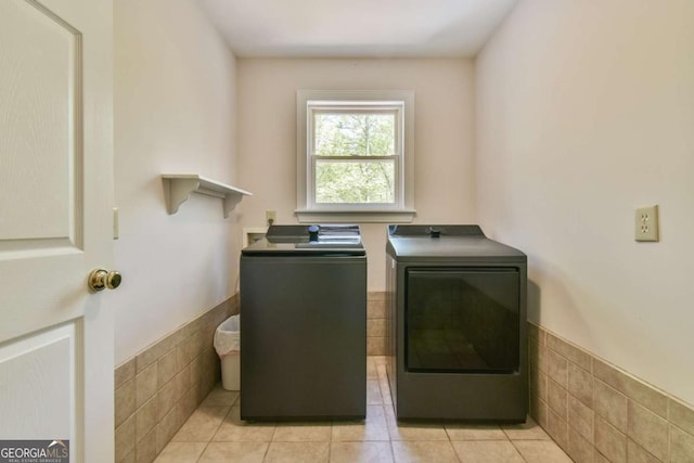clothes washing area featuring washing machine and dryer, laundry area, tile walls, and a wainscoted wall