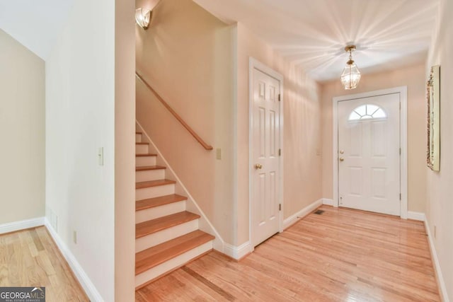 foyer entrance featuring baseboards, light wood finished floors, and stairs