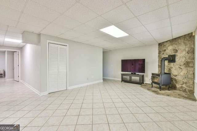 below grade area with light tile patterned floors, a wood stove, a paneled ceiling, and baseboards
