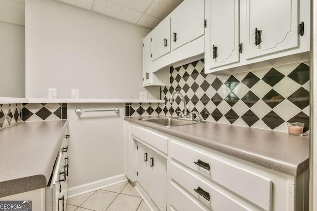 kitchen with light tile patterned floors, a sink, a paneled ceiling, white cabinetry, and decorative backsplash