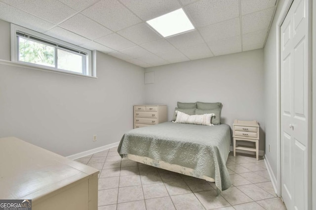 bedroom with a closet, light tile patterned flooring, baseboards, and a drop ceiling