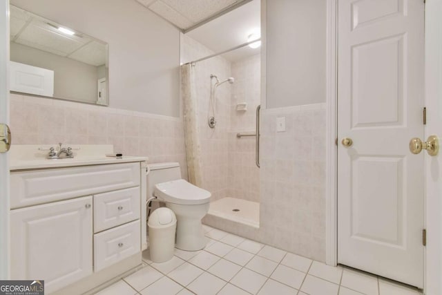 full bath featuring tile patterned floors, a wainscoted wall, toilet, tiled shower, and tile walls
