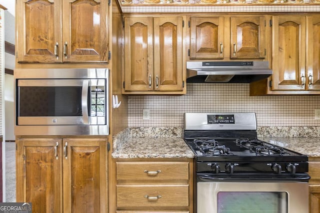2237 W Elm St, Wrightsville, GA 31096 - kitchen featuring brown cabinetry, under cabinet range hood, tasteful backsplash, and stainless steel appliances
