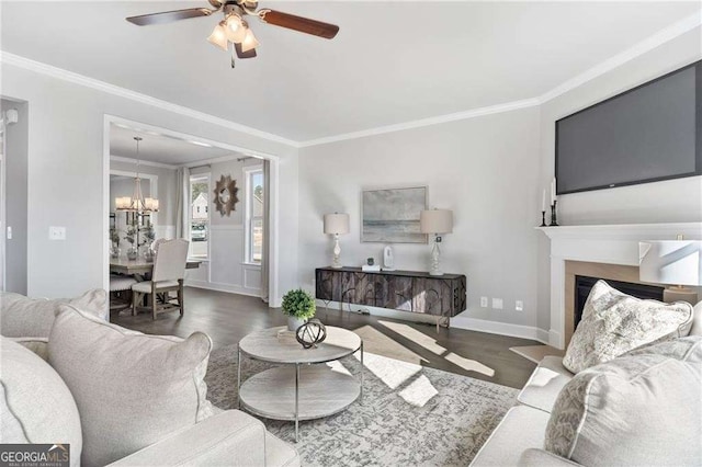 living room featuring baseboards, ornamental molding, a fireplace, wood finished floors, and ceiling fan with notable chandelier