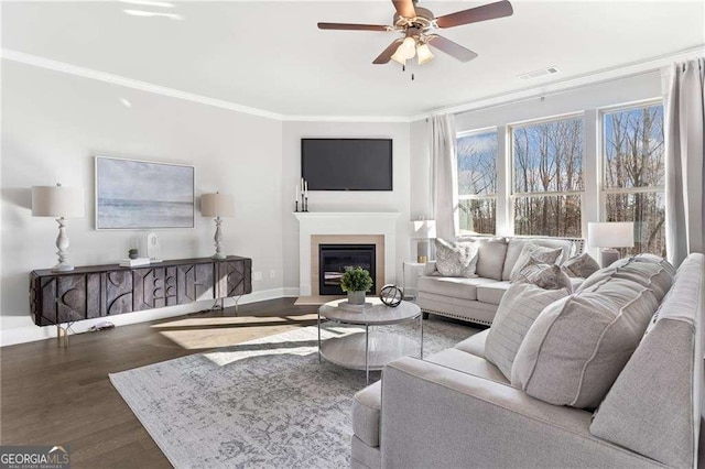 living room featuring baseboards, ceiling fan, crown molding, wood finished floors, and a glass covered fireplace