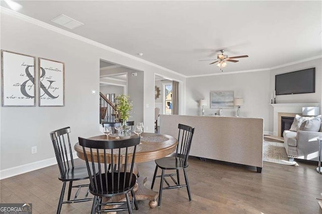 dining room with dark wood-style flooring, ornamental molding, ceiling fan, and a glass covered fireplace